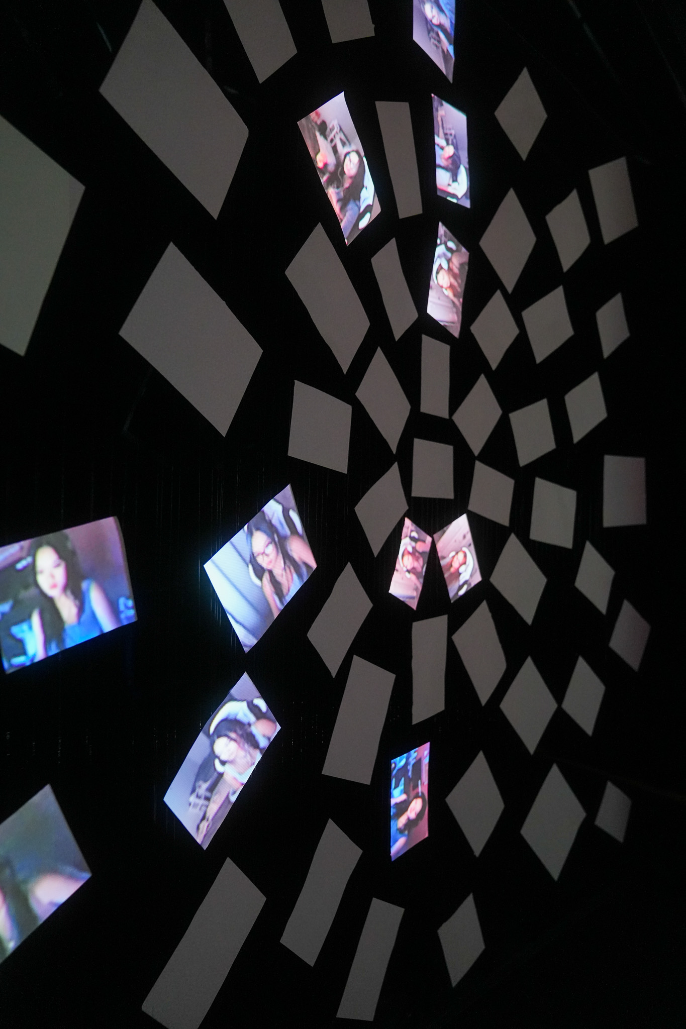 Multiple screens and blank panels are arranged in a spiral pattern on a dark background, displaying various images of people. The arrangement creates a dynamic, abstract visual effect.
