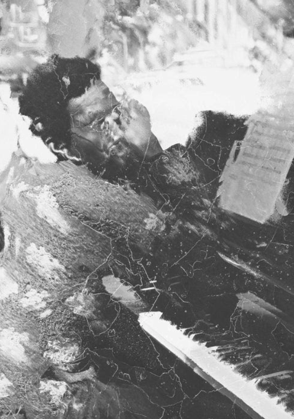 A person sits at a piano, covering their face with one hand while looking at sheet music. The image is black and white with a scratched, textured effect, giving it an abstract, distressed appearance.